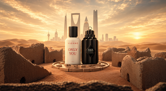 Vierro Only You and Black Forest perfume bottles displayed on a stone pedestal amid ancient desert ruins, with golden sand dunes and the Saudi Arabian skyline at sunset.
